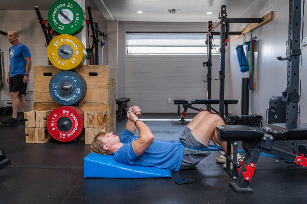 Braden Johnson demonstrating banded lumbar traction at Smith Performance Center in Tucson, aiding clients with low back pain in regaining movement confidence and tissue capacity.
